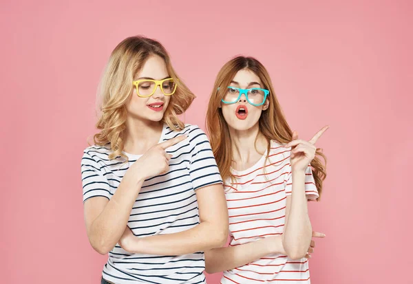 티셔츠에 유행하는 안경을 끼고 핑크 색 배경을 가진 두 여성 이 함께 대화를 나누는 우정 — 스톡 사진