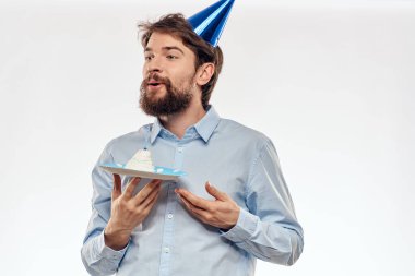 Sakallı bir adam arka planda hafif bir doğum gününde elinde pasta tutuyor.