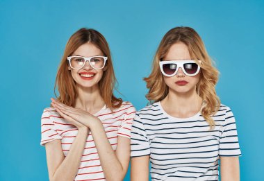 Çizgili tişörtlü iki neşeli kız arkadaş. Güneş gözlükleri, arkadaşlığa sarılıyor. 