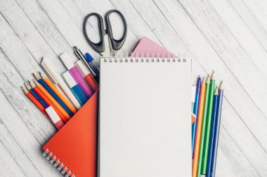 Not defteri boyalı kalemler ve keçeli kalemler okul ofisindeki ahşap masaya.