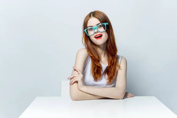 Bella donna in occhiali blu seduto a tavola labbra rosse sorriso sguardo attraente — Foto Stock