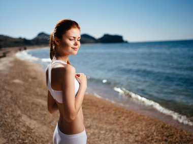 Beyaz mayo giymiş bir kadın plaj adası manzarası güneşinde yürüyor.