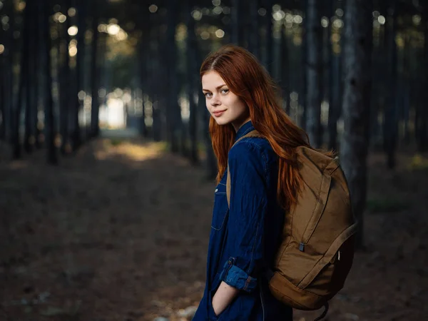 Happy traveler with a backpack on her back is resting in nature in a pine forest