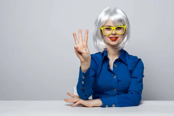 Vrolijk mooi vrouw in een witte pruik gebaren met haar vingers aan de tafel blauw shirt — Stockfoto