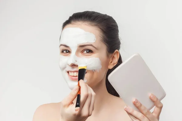 Morena desnuda hombros aplicando crema cepillo en la cara —  Fotos de Stock