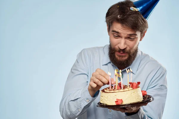 Un hombre con una camisa con un pastel en las manos y una gorra festiva en la cabeza — Foto de Stock