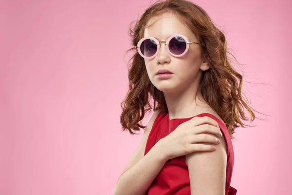 쾌활 한 어린 소녀어린 시절검은 안경을 쓴 빨간 드레스를 입은 핑크 색 배경 — 스톡 사진
