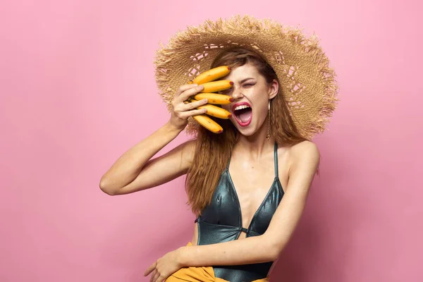 Kvinna i stranden halm hatt bananer håller frukt Exotisk baddräkt rosa bakgrund — Stockfoto