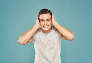 Tişört giymiş neşeli bir adam elleri mavi arka planda hareketler yapar.