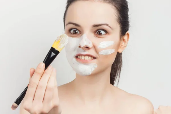 Привлекательная брюнетка наносит маску на лицо с уходом за кожей кисти — стоковое фото