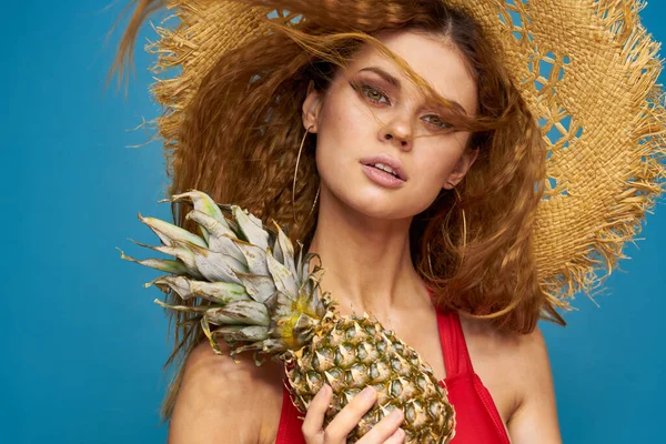Kvinna i en halmhatt med ananas i händerna vågigt hår exotiska frukter du sommar blå bakgrund semester — Stockfoto