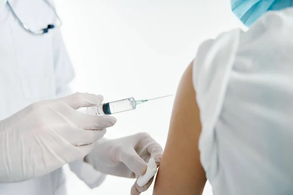 Лікар в захисних рукавичках вводить вакцину в плече пацієнта жінки в лікарняній ковдрі — стокове фото