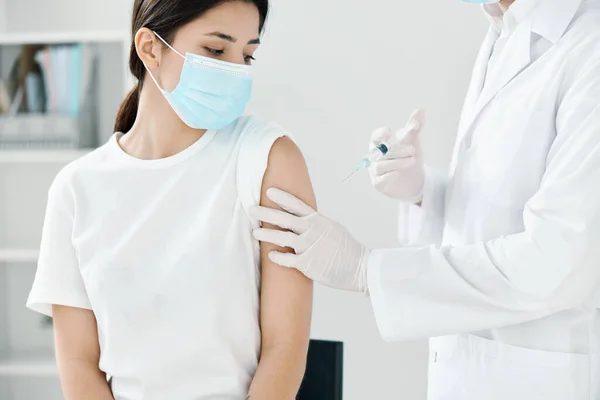 Orvos orvosi köpenyben és maszkban befecskendez egy nőt a vállba kovid védőoltás — Stock Fotó