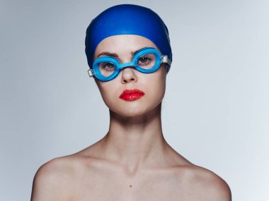 Mavi gözlüklü, yüzme şapkalı, omuzları açık bir kadın.