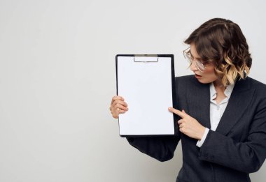 Belgeli bir iş kadını, elleri arka planda ve yüzünde gözlüklerle el kol hareketi yapar.