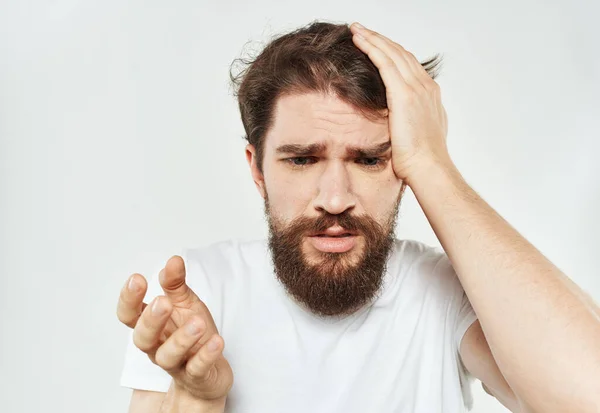 Emotionele man in een T-shirt raakt zijn hoofd met zijn handen op een lichte achtergrond bijgesneden uitzicht — Stockfoto