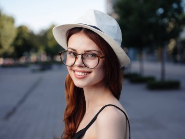Beyaz şapkalı ve gözlüklü mutlu kadın sokaklarda yürüyor.