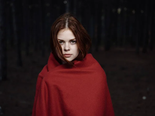 Μια παγωμένη γυναίκα με μια κόκκινη κουβέρτα στους ώμους της στο δάσος. — Φωτογραφία Αρχείου