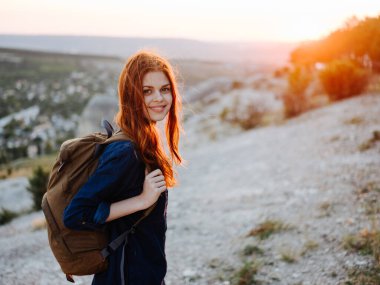 Sırtında sırt çantasıyla dağlarda bir kadın. Kızıl saçlı gün batımı.