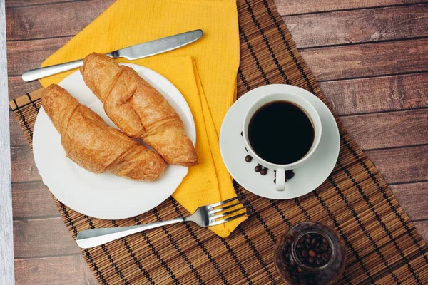 Croissants frescos em uma mesa de pires que define copo de café da manhã com bebidas — Fotografia de Stock