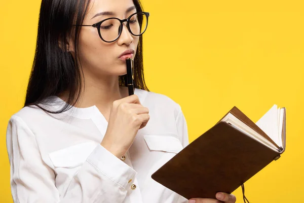 Mooi brunette met bril houden van een notebook in de handen van studenten leren gele achtergrond — Stockfoto