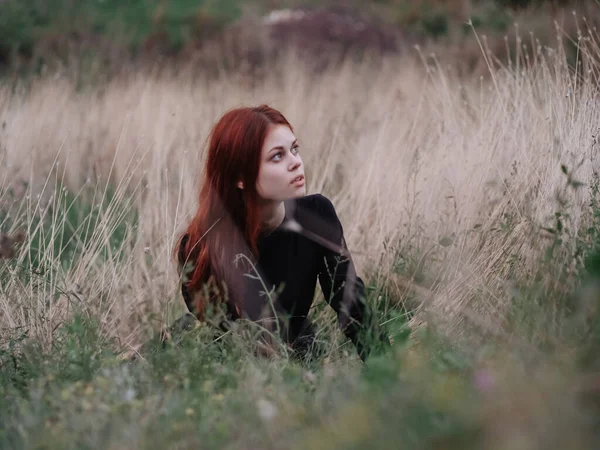 Femme aux cheveux roux dans une robe noire se trouve dans la forêt sur l'herbe sèche dans la nature — Photo
