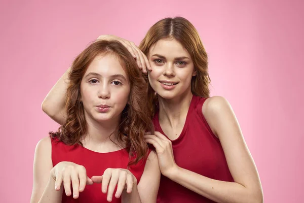 Mãe e filha em vestidos vermelhos abraços diversão grimace infância alegria rosa fundo — Fotografia de Stock