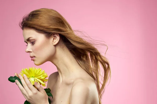 Menina bonita com uma flor amarela em um fundo rosa nua ombros maquiagem — Fotografia de Stock