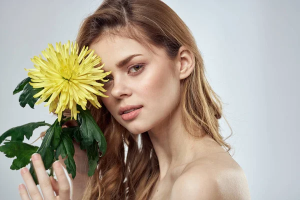 Retrato de una hermosa mujer con una flor amarilla sobre un fondo claro encantadora sonrisa modelo pelo rojo — Foto de Stock