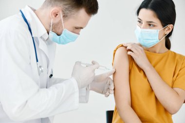 Doktor asistanı, tıbbi maske takan bir kadının omzuna iğne yapıyor.