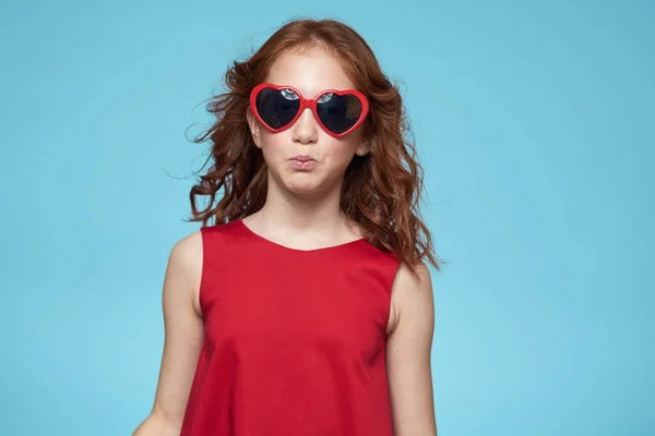 Niña alegre con gafas de sol en forma de un vestido rojo corazón fondo azul — Foto de Stock