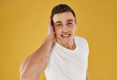 Beyaz tişörtlü enerjik bir adam elini sarı arka planda tutuyor.