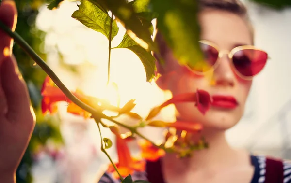 Vacker kvinna i glasögon nära röda blommor på gatan och röd solklänning randig t-shirt — Stockfoto