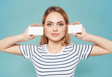 Mavi arka planda ve çizgili tişörtte farklı boylarda kartviziti olan bir kadın.