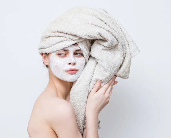 Wanita dengan handuk di kepala bahu telanjang topeng putih di perawatan kulit wajah — Stok Foto