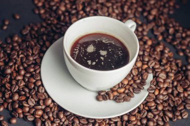 Kahve çekirdekleri ve bir fincan beyaz çay tabağı üzerine koyu arkaplan içeceği.