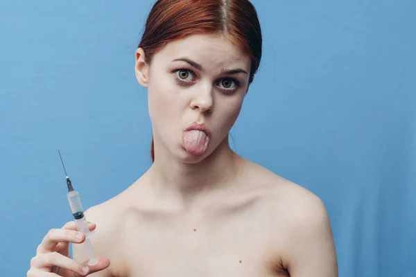 Emotional red-haired woman on blue background holding syringe in hand cropped view — Stock Photo, Image