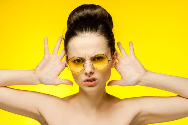 Çıplak omuzlu bir kadın. Sarı gözlükler. Yüzüne yakın eller. — Stok fotoğraf