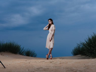 Sundress giymiş bir kadının uzun bir portresi ve kumsalda kırmızı sandaletler.