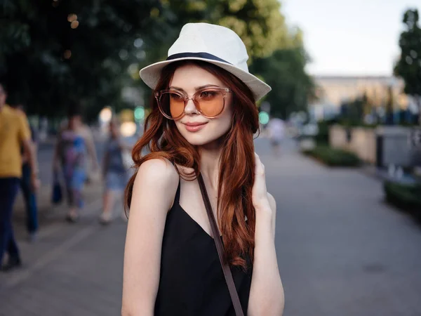 Donna alla moda in un vestito nero e in un cappello bianco stanno riposando nella natura per strada nel parco — Foto Stock