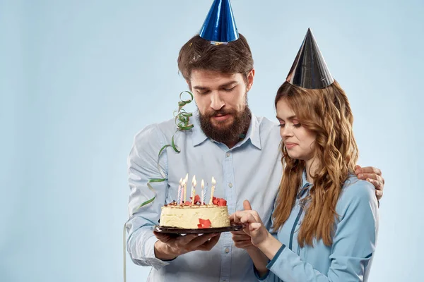 Birthday man woman in party hats on a blue background and cake with candles