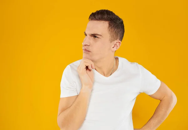 A man in a white T-shirt touches his face with his hand on a yellow background of emotion — Stock Photo, Image