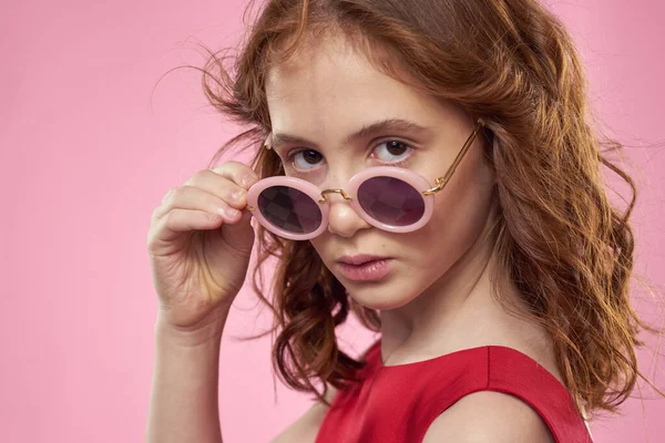 Девушка с вьющимися волосами темные круглые очки весело красное платье розовый фон — стоковое фото
