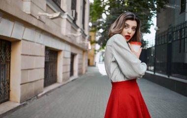 Kırmızı etekli şık sarışın kadın kaldırım parkının yanında duruyor.