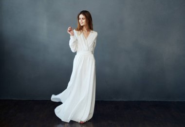 Beyaz elbiseli çekici bir kadının portresi. Gri bir arka planı var.