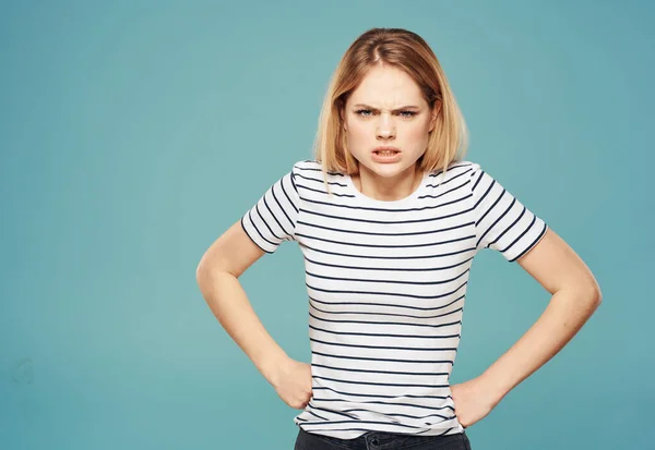 Nervous woman in a striped T-shirt gestures with her hands on a blue background