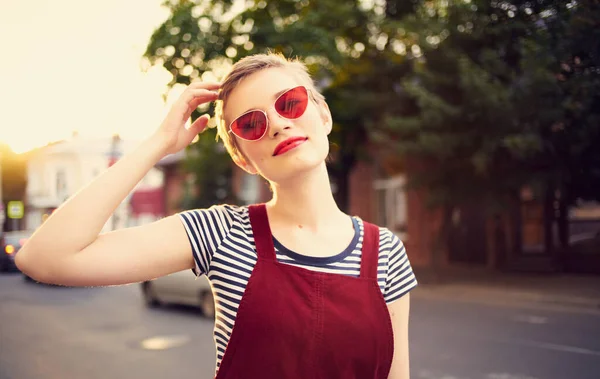 Romantisk kvinna i solklänning och röda glasögon promenader längs stadens gata på sommaren — Stockfoto