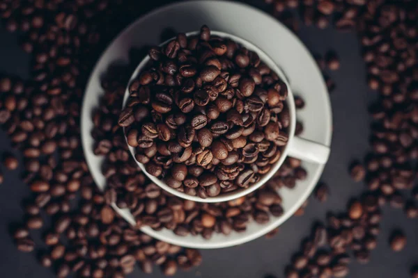 Granos de café en una taza y platillos blancos fondo gris de cerca — Foto de Stock