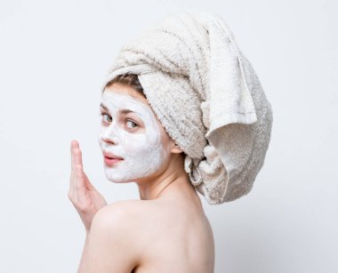 Kafasında havluyla mutlu bir kadın. Çıplak omuzları nemlendirici, yüz maskesi.