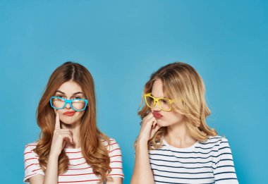 Moda stüdyosunda sosyalleşen iki kız arkadaş mavi arka planda.